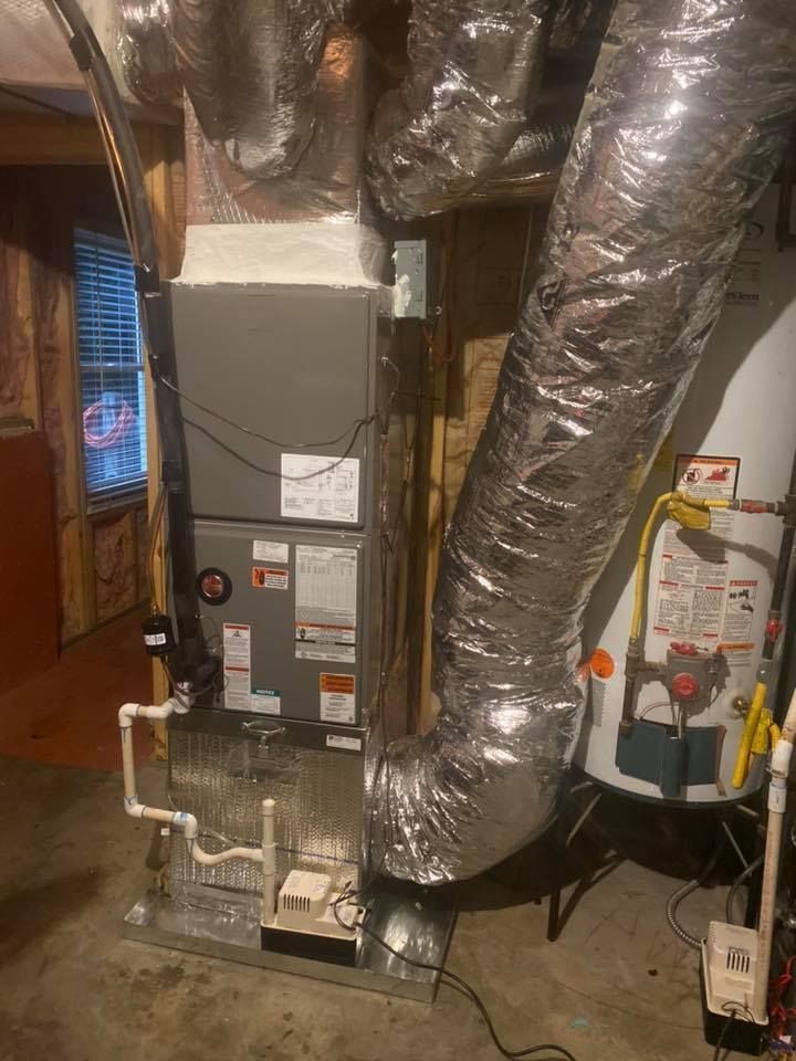 Basement HVAC furnace with silver ducts and white PVC pipes in a utility room