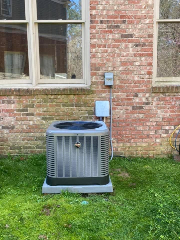 Outdoor AC unit beside a brick house wall beneath a window and electrical box