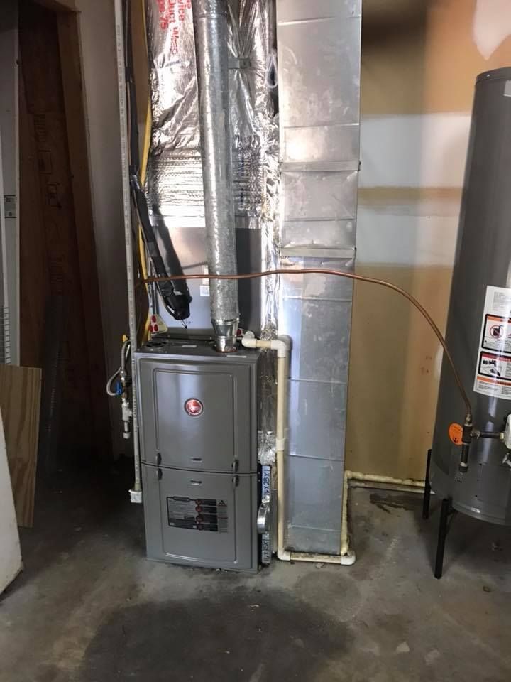 Basement furnace beside metal ductwork and a water heater in a utility room