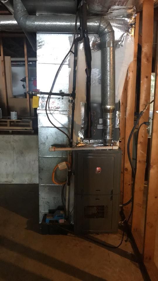 Basement furnace and ductwork with exposed pipes and silver insulation next to a wall.