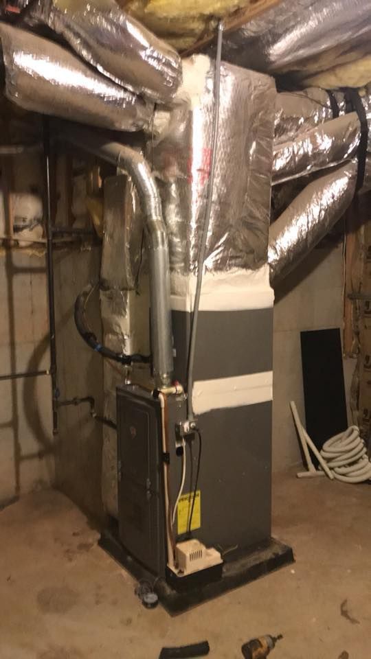 Basement HVAC furnace with silver ductwork and pipes on a concrete floor