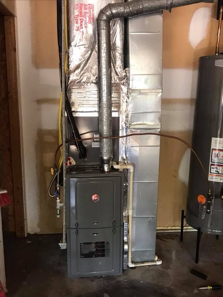 Basement furnace and ductwork with metal ventilation pipes and water heater next to HVAC unit