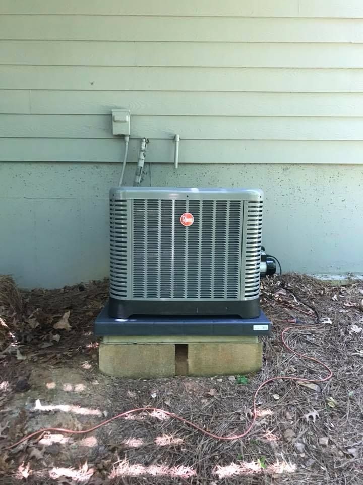 Outdoor air conditioner unit beside a house wall, set on concrete blocks with a utility meter above it