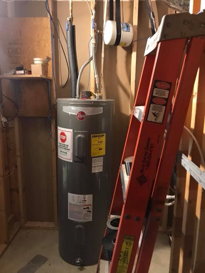 Water heater in a utility closet beside a red ladder and exposed pipes and wiring.