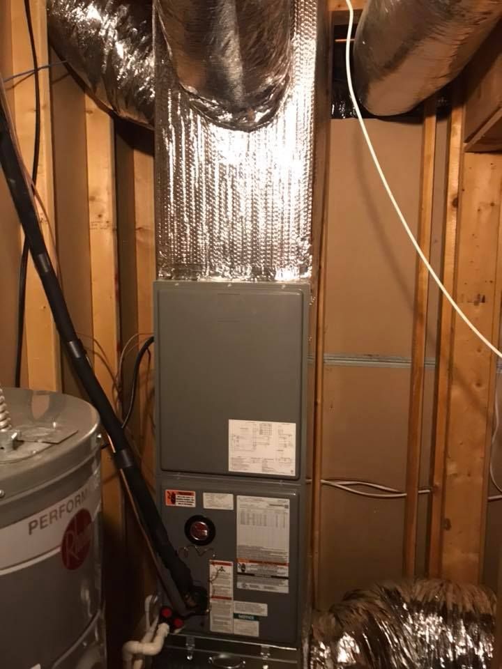 Furnace unit in an unfinished basement with exposed wooden studs and ductwork.
