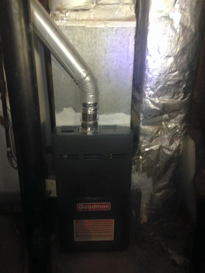 Furnace unit with a silver duct in a basement or utility room, surrounded by insulated walls.