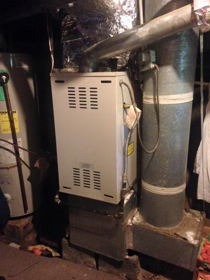 Basement furnace and ductwork with beige HVAC unit beside insulated metal vents