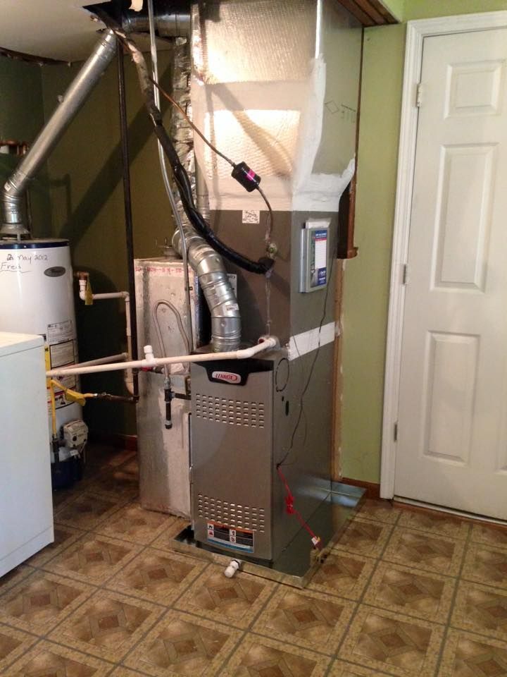 Basement utility room with a furnace, water heater, exposed ducts, and a white door on the right