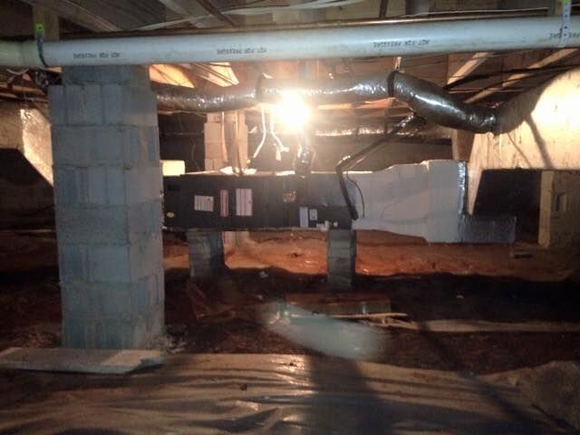 Crawlspace with exposed beams, ductwork, cinder blocks, and bright light shining from the back.