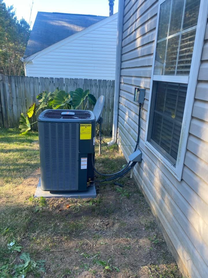 Outdoor air conditioner unit beside a house wall and window, next to a wooden fence.
