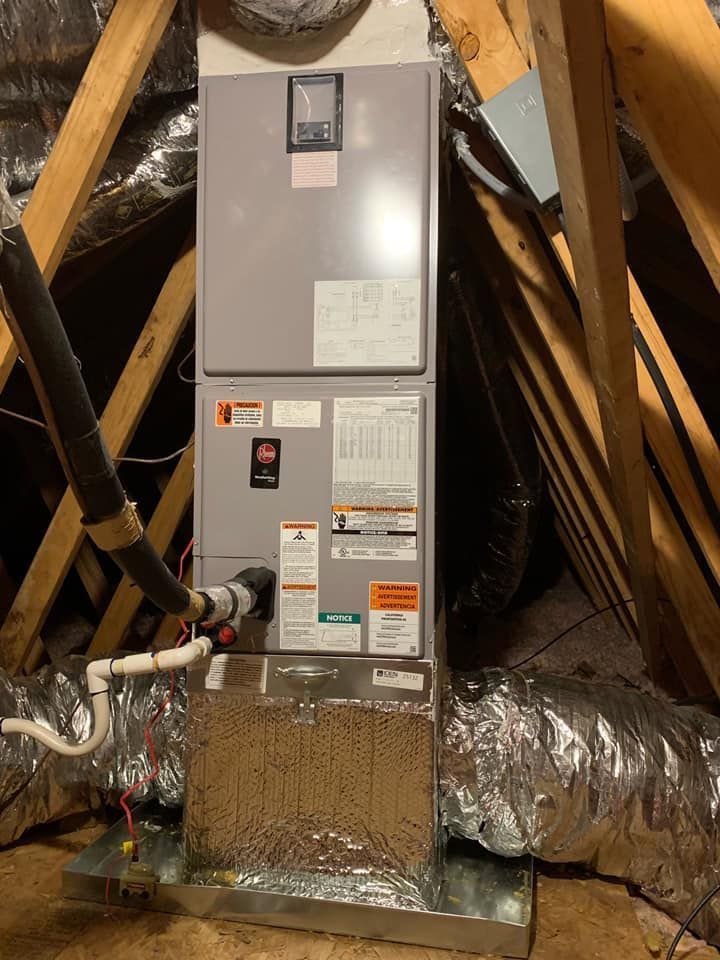 Gray HVAC furnace in attic with insulated ducts and exposed wooden rafters