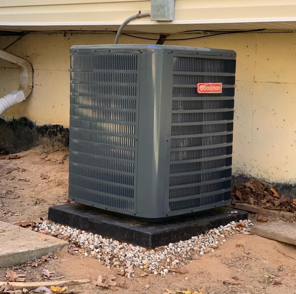 Gray outdoor HVAC unit beside a house, set on a black pad with gravel around it.