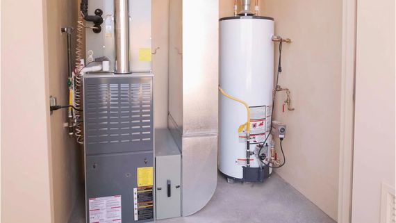 Utility closet with furnace and white water heater beside exposed pipes and vents