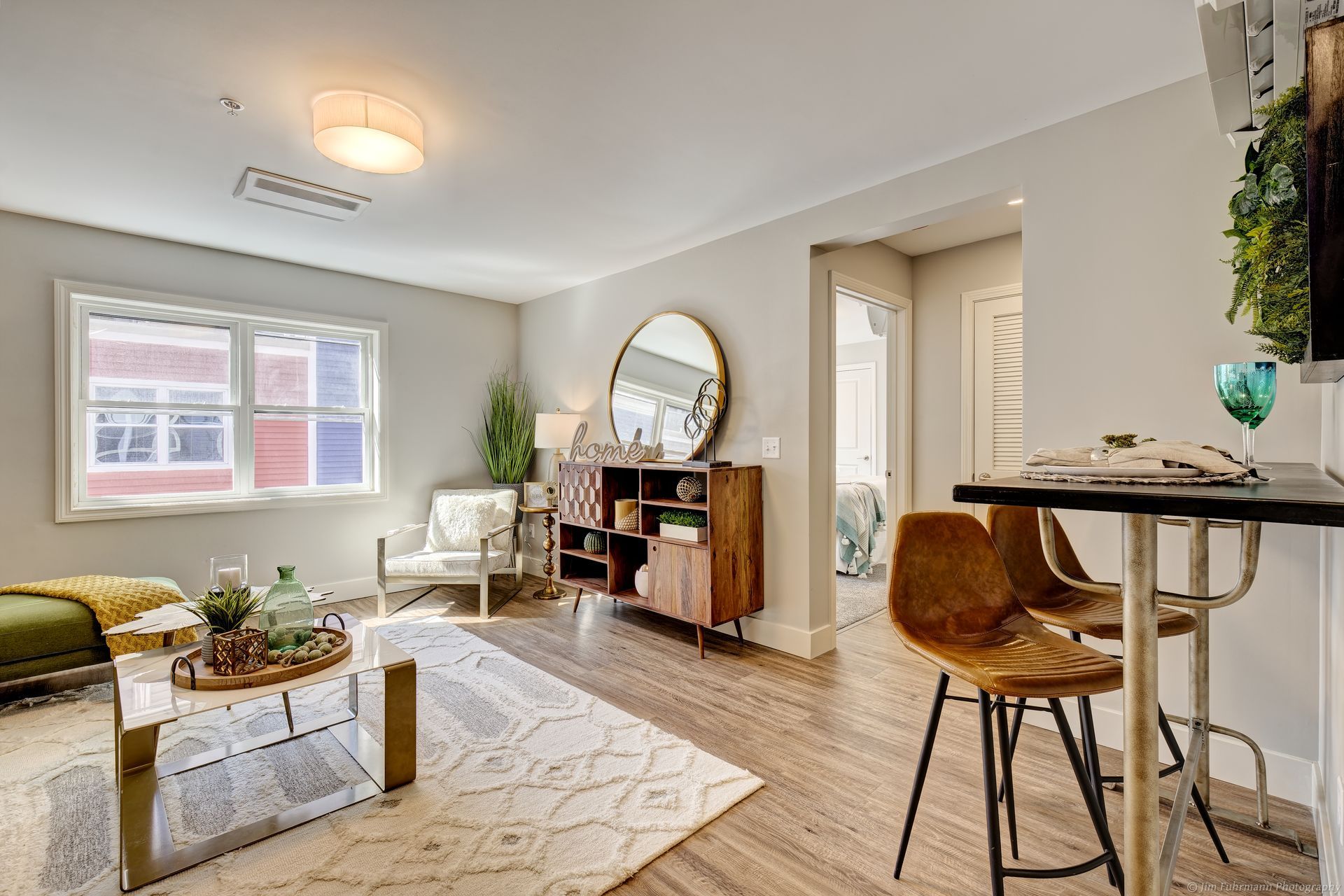 A modern living space with a window, rug, seating, wooden cabinet, and a small breakfast bar with stools.