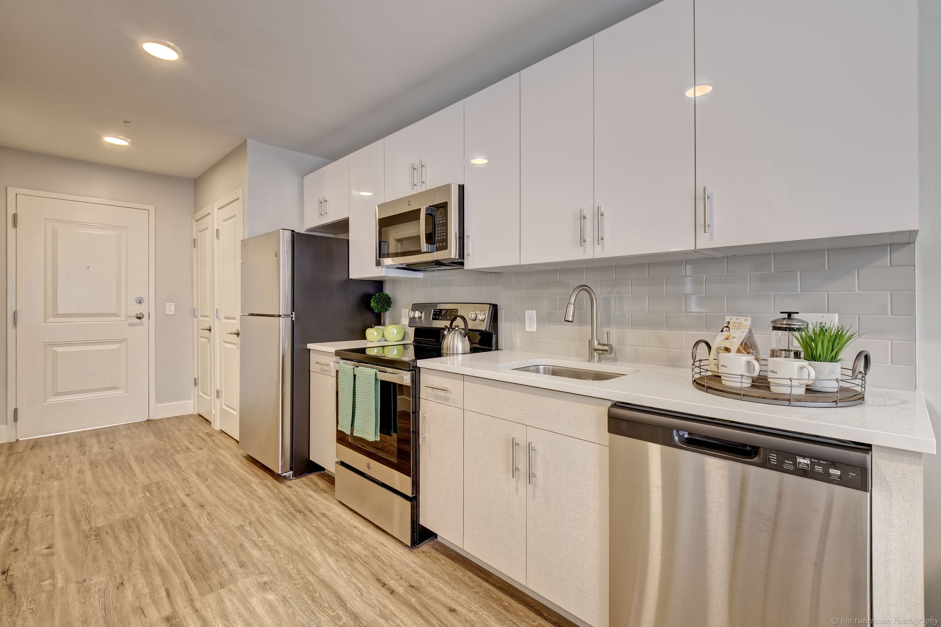 Modern, white kitchen with stainless steel appliances, light wood-look floor, and white glossy cabinets.