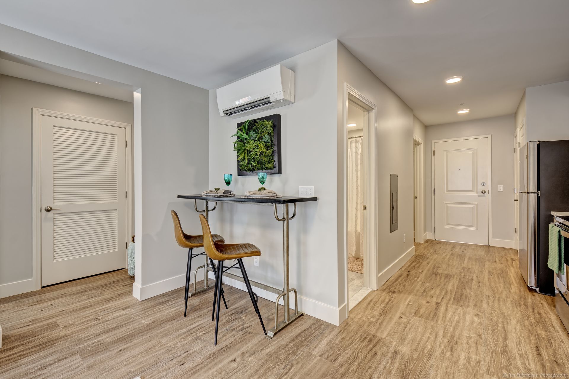 A brightly lit interior view with a breakfast bar, two stools, and a hallway leading to doorways and appliances.