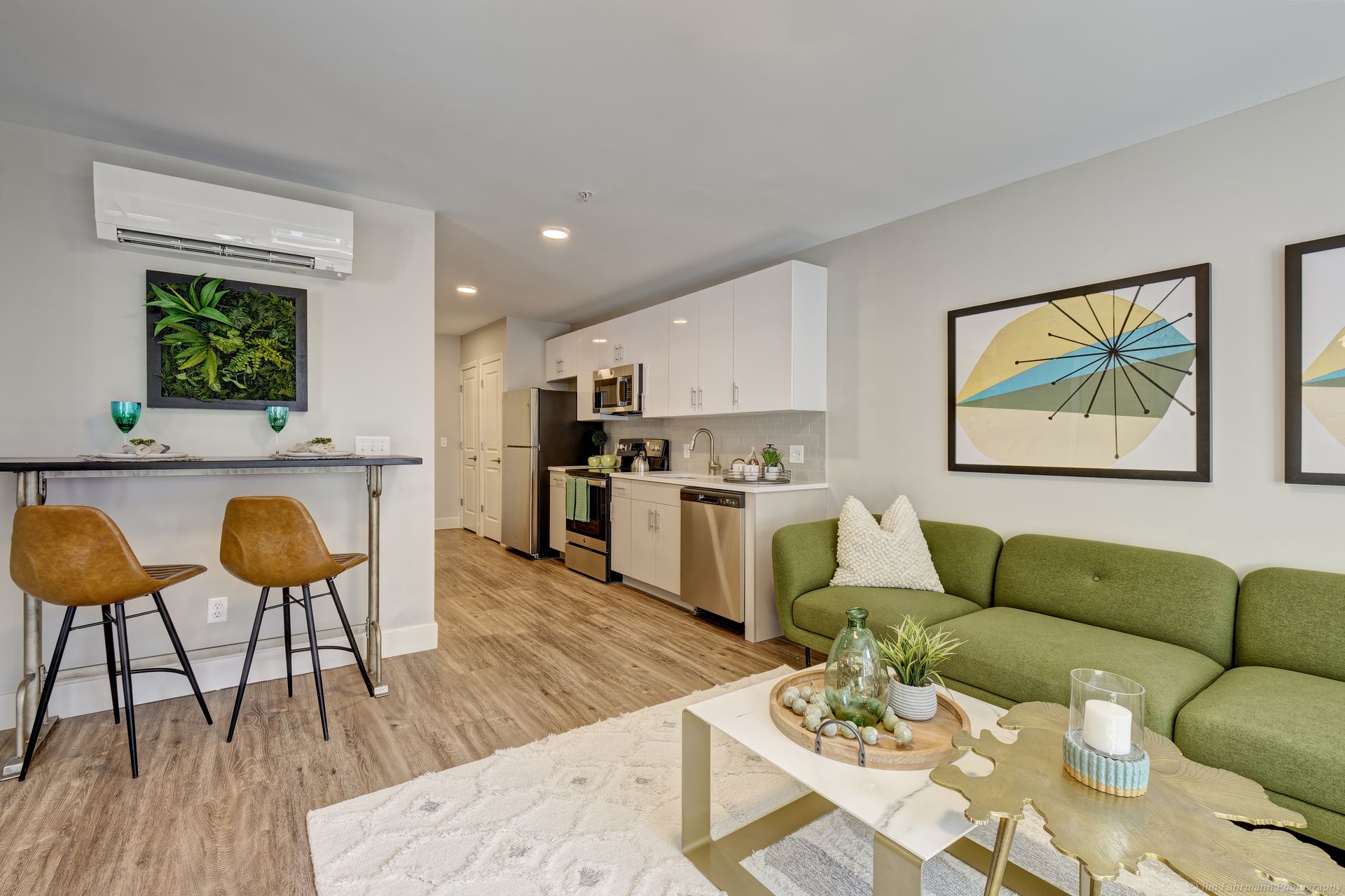 Green sectional sofa and white armchair in a living room with abstract art and a window, light wood floors, and a shag rug.