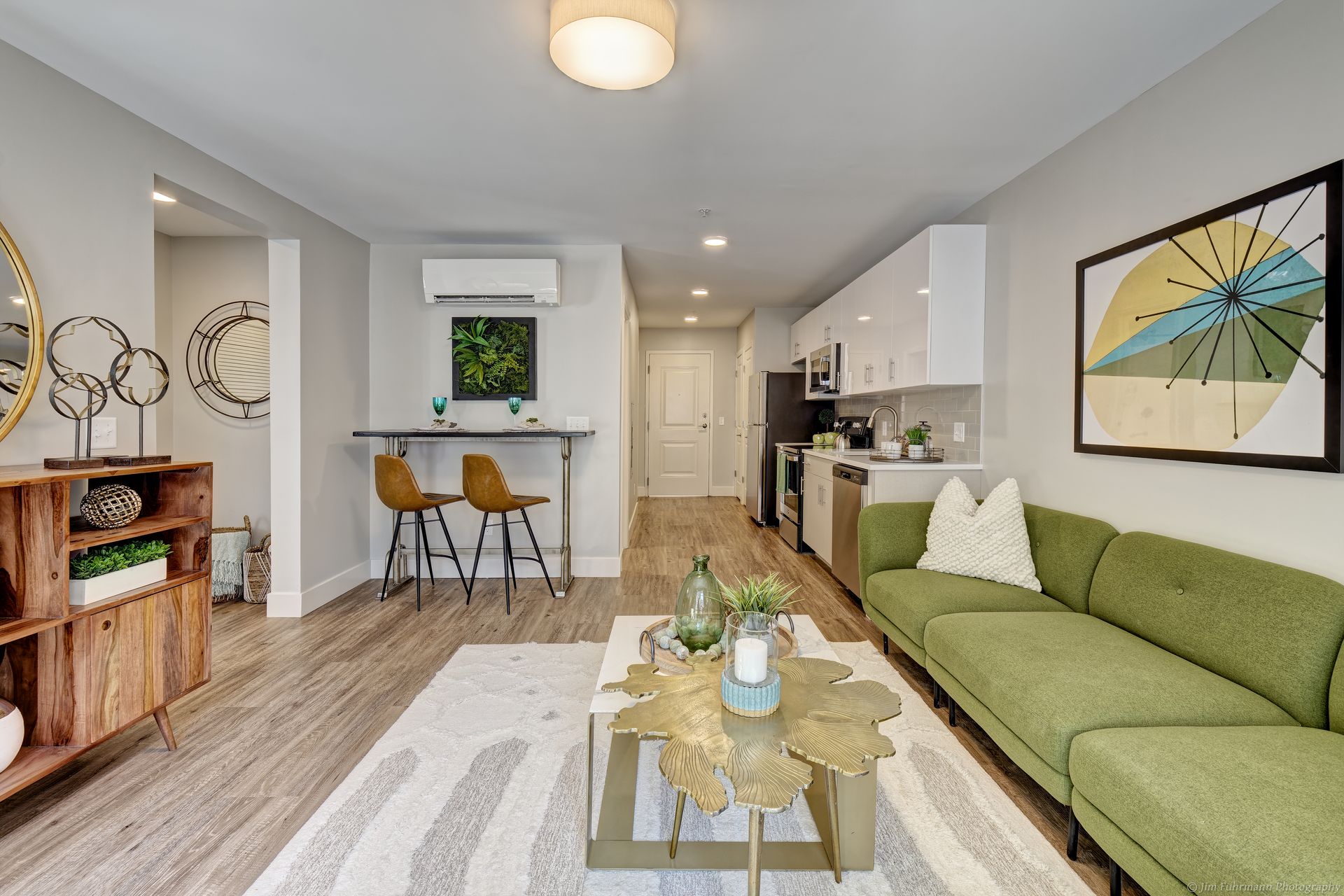 Modern apartment living room with green sofa, wooden coffee table, and open kitchen with white cabinets.