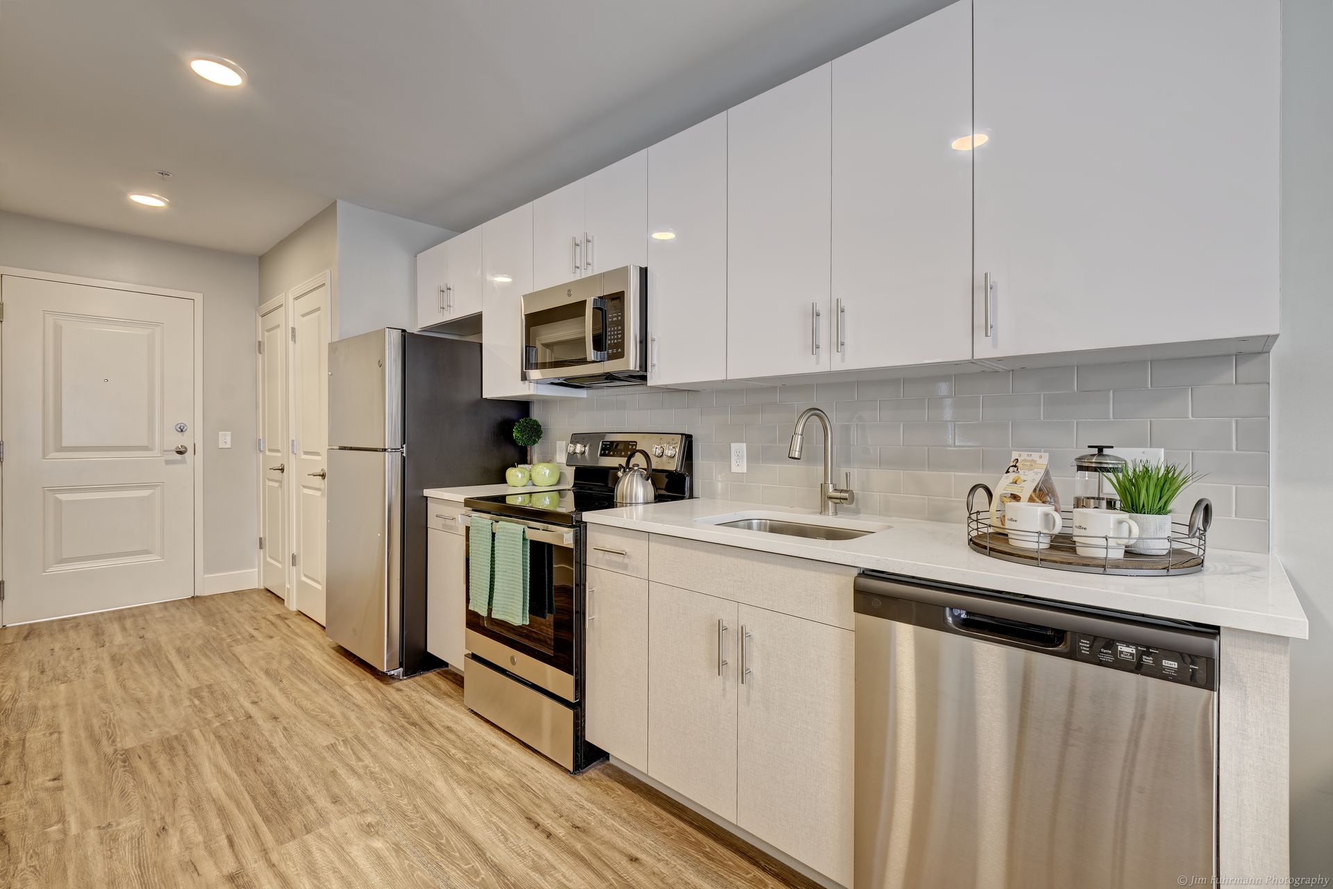 Modern kitchen with white cabinets, stainless steel appliances, and wood-look flooring.