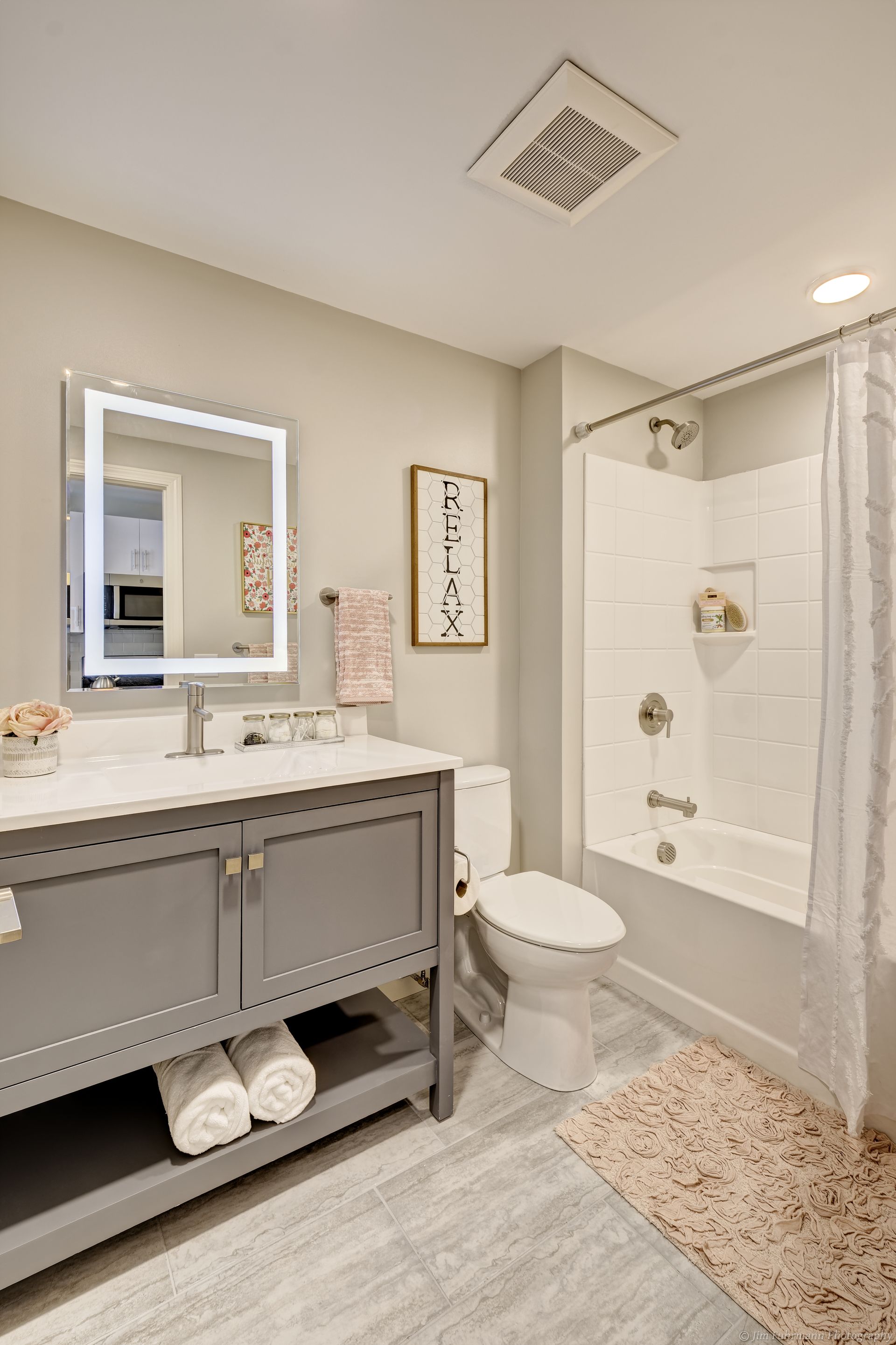 Gray and white bathroom with a vanity, toilet, shower/tub, and decorative rug.
