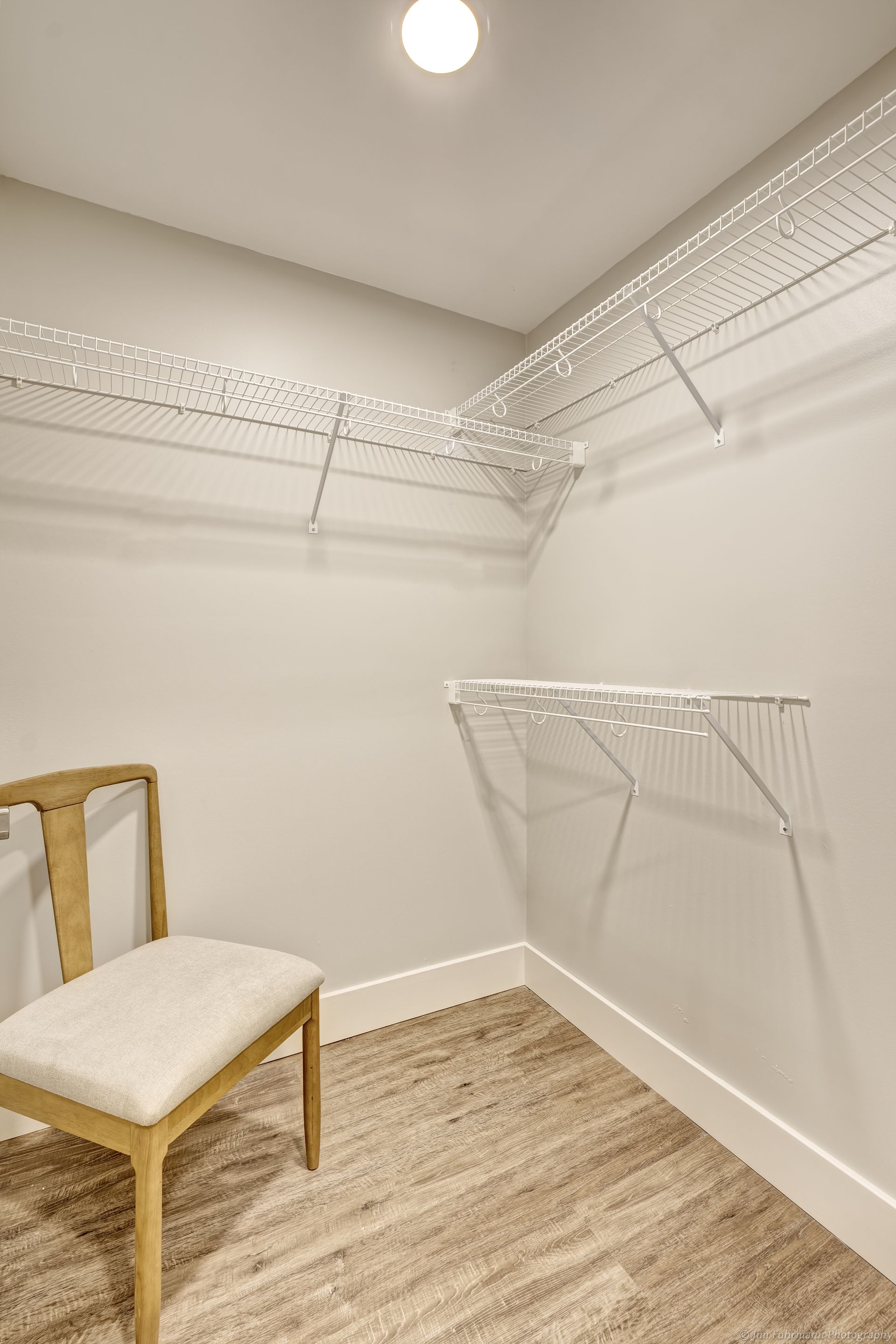 A small walk-in closet with white wire shelving, a wooden chair, and a beige rug.