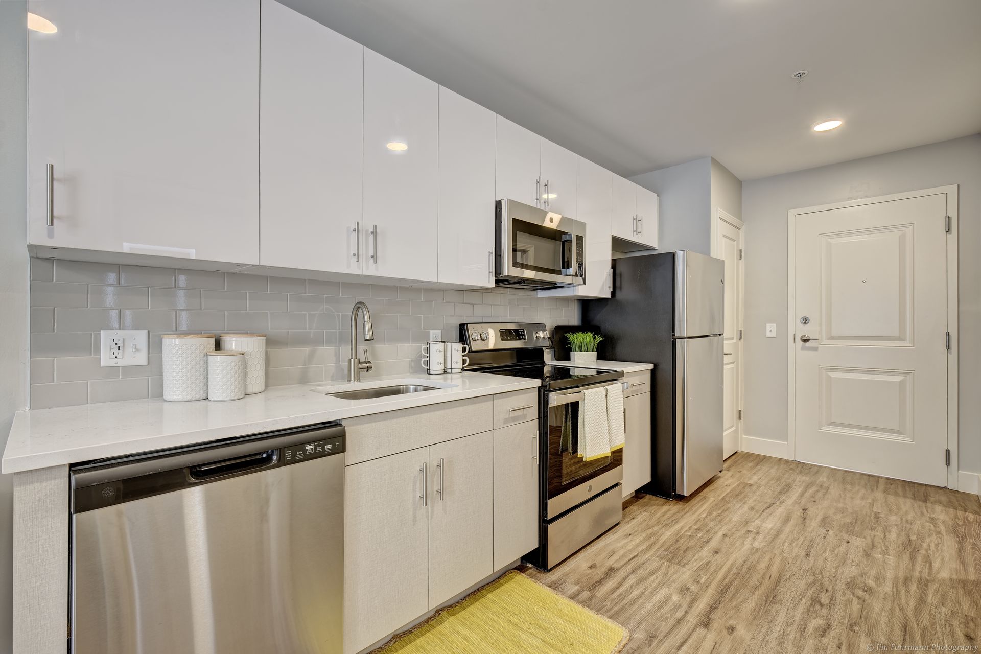 Modern kitchen with white cabinets, stainless steel appliances, and wood-look flooring.