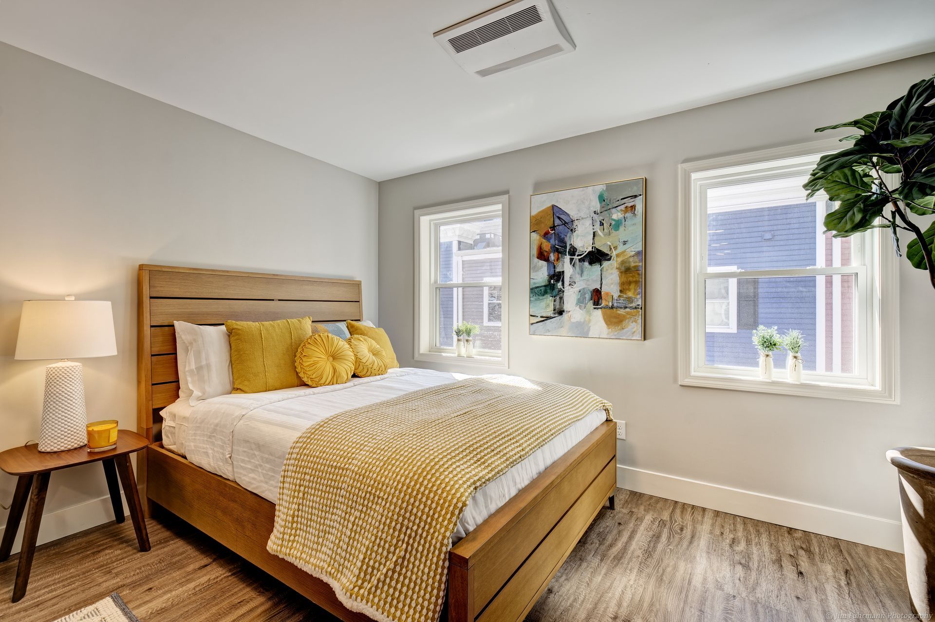 A bedroom with a bed , lamps , and two windows.