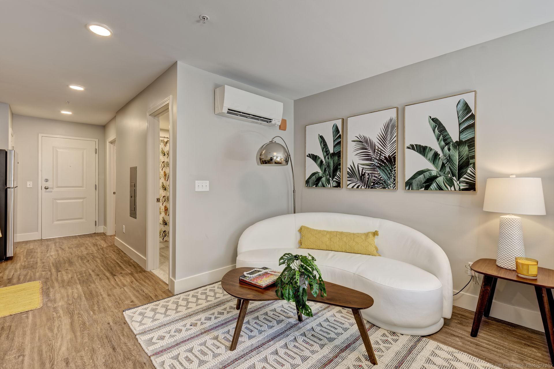 Modern living room with white curved sofa, art prints of plants, wooden side table, and patterned rug.