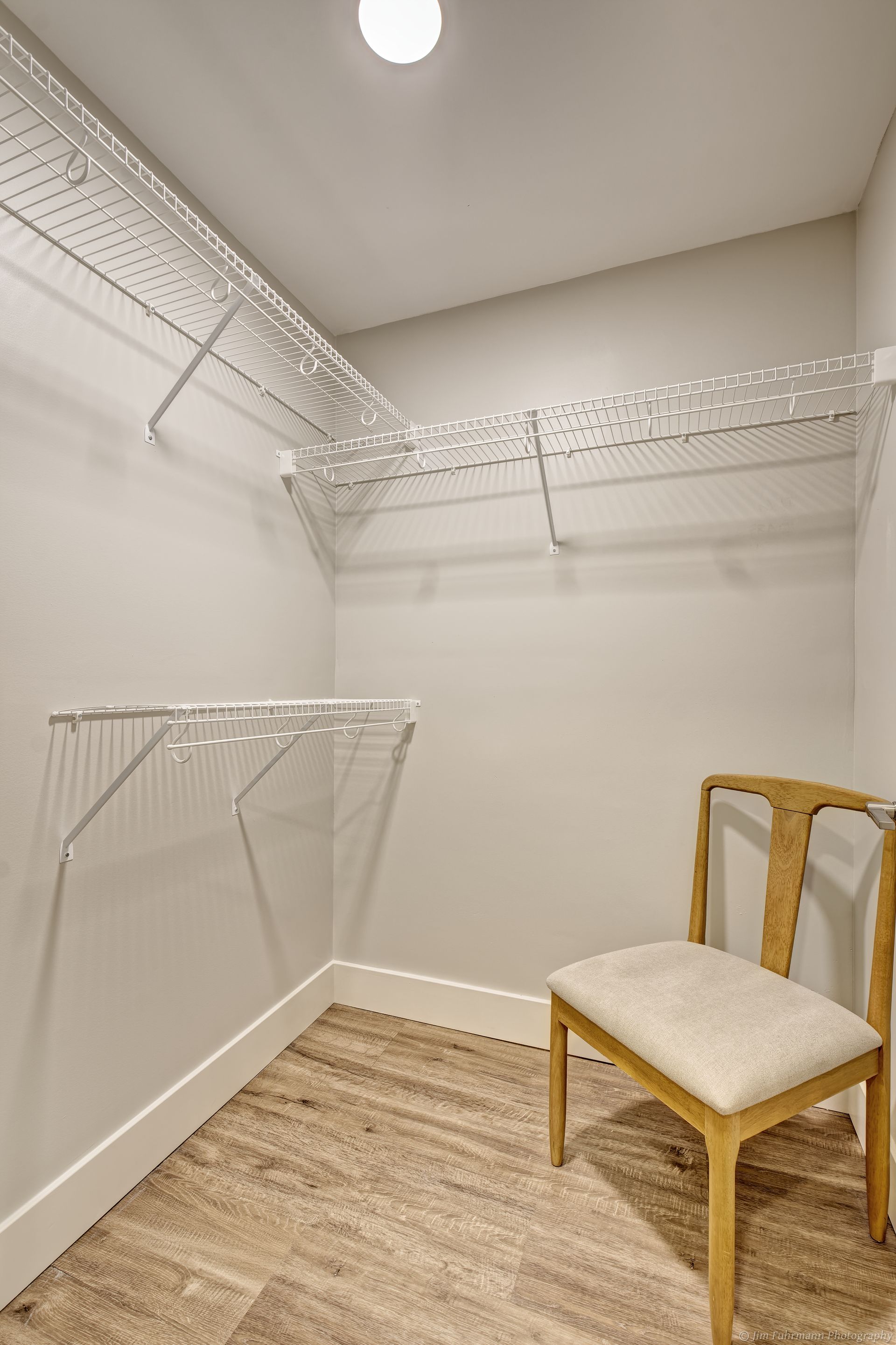 Empty walk-in closet with wire shelving, a chair, and light flooring. White walls and trim.