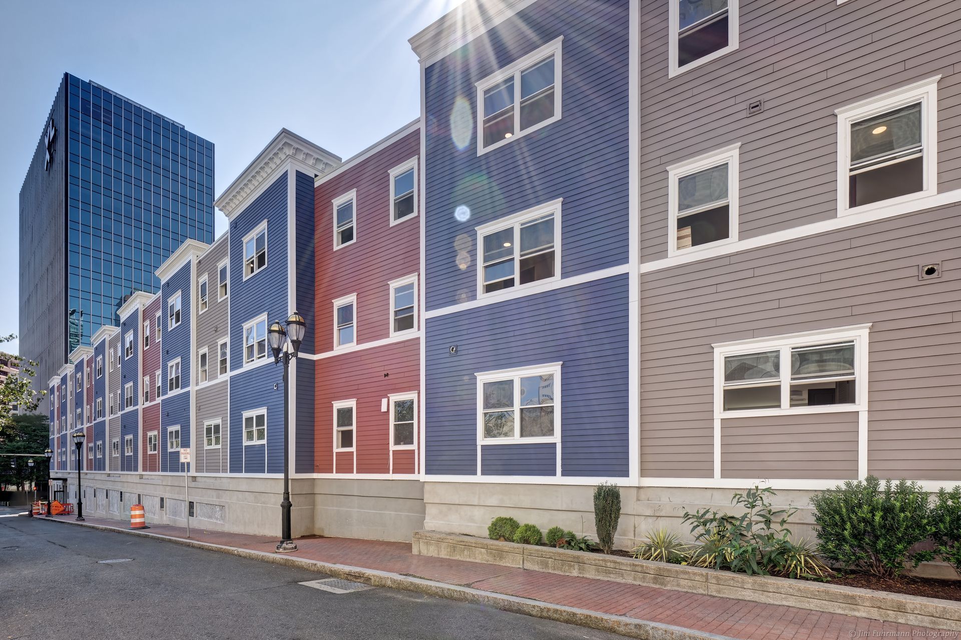 Colorful apartment building facade on a city street with a large blue skyscraper in the background. The building has blue, red, and gray panels.