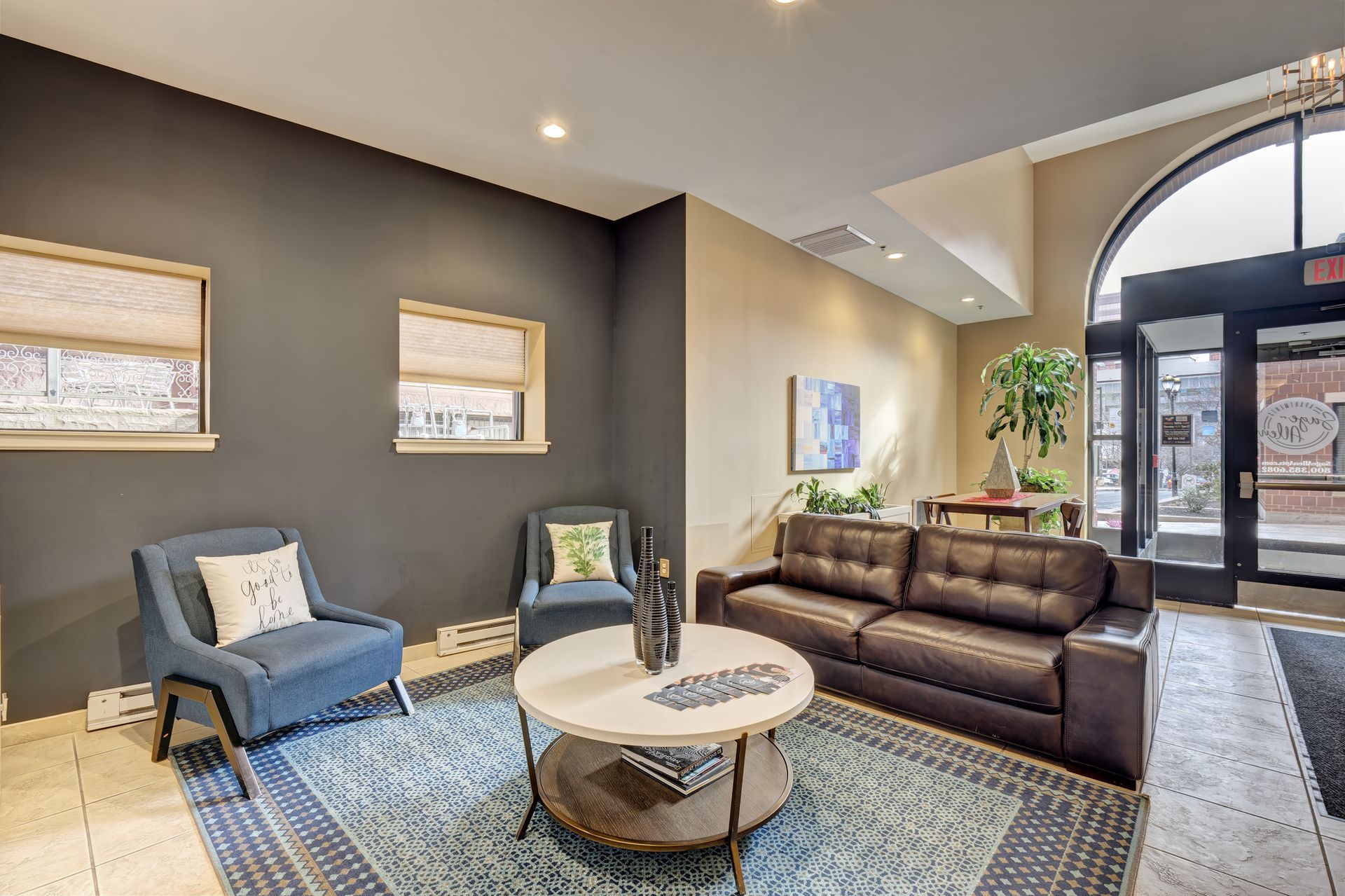 A modern waiting area with blue armchairs, a brown sofa, and a round coffee table on a blue rug. Dark gray and tan walls.