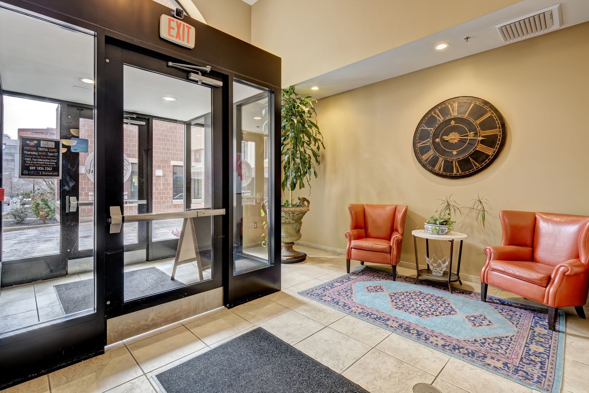 An entryway with two orange armchairs, a rug, and a large clock on the wall. Glass doors lead outside.