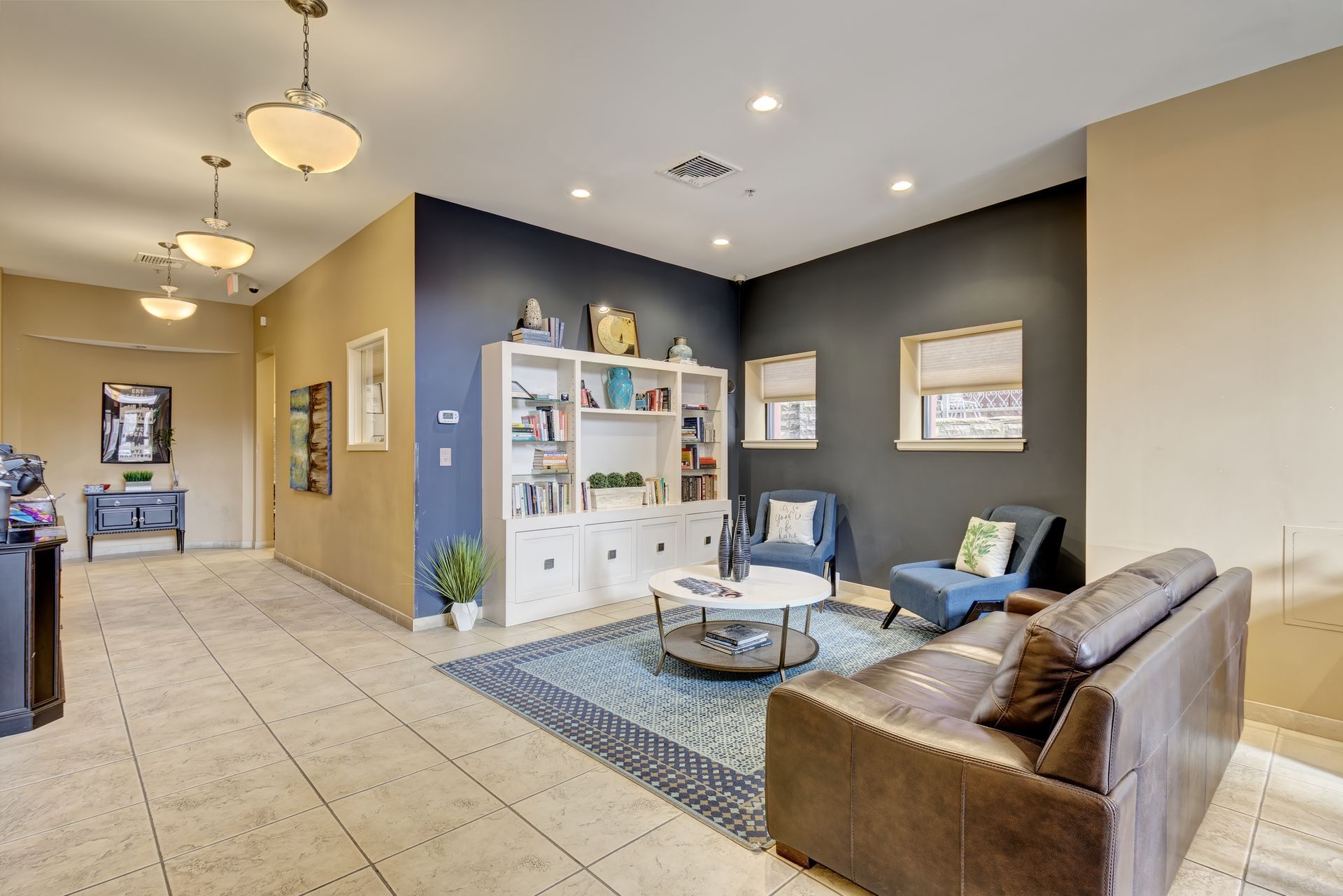 Cozy office waiting area with blue accent wall, brown leather sofa, bookshelves, and a blue patterned rug.