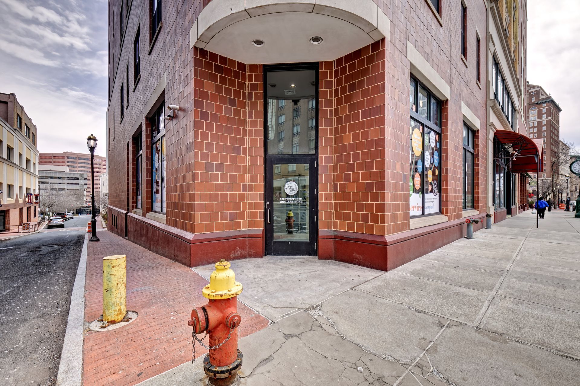 Brick building corner with entrance under a curved white overhang. Red fire hydrant and yellow post stand near the entrance.