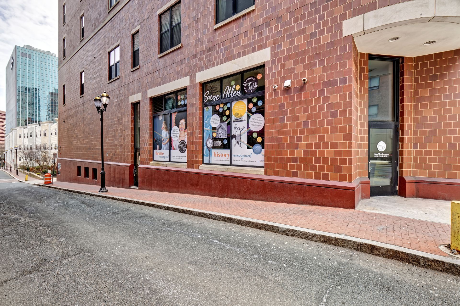 Brick building exterior with storefront and street. A lamppost stands in front.