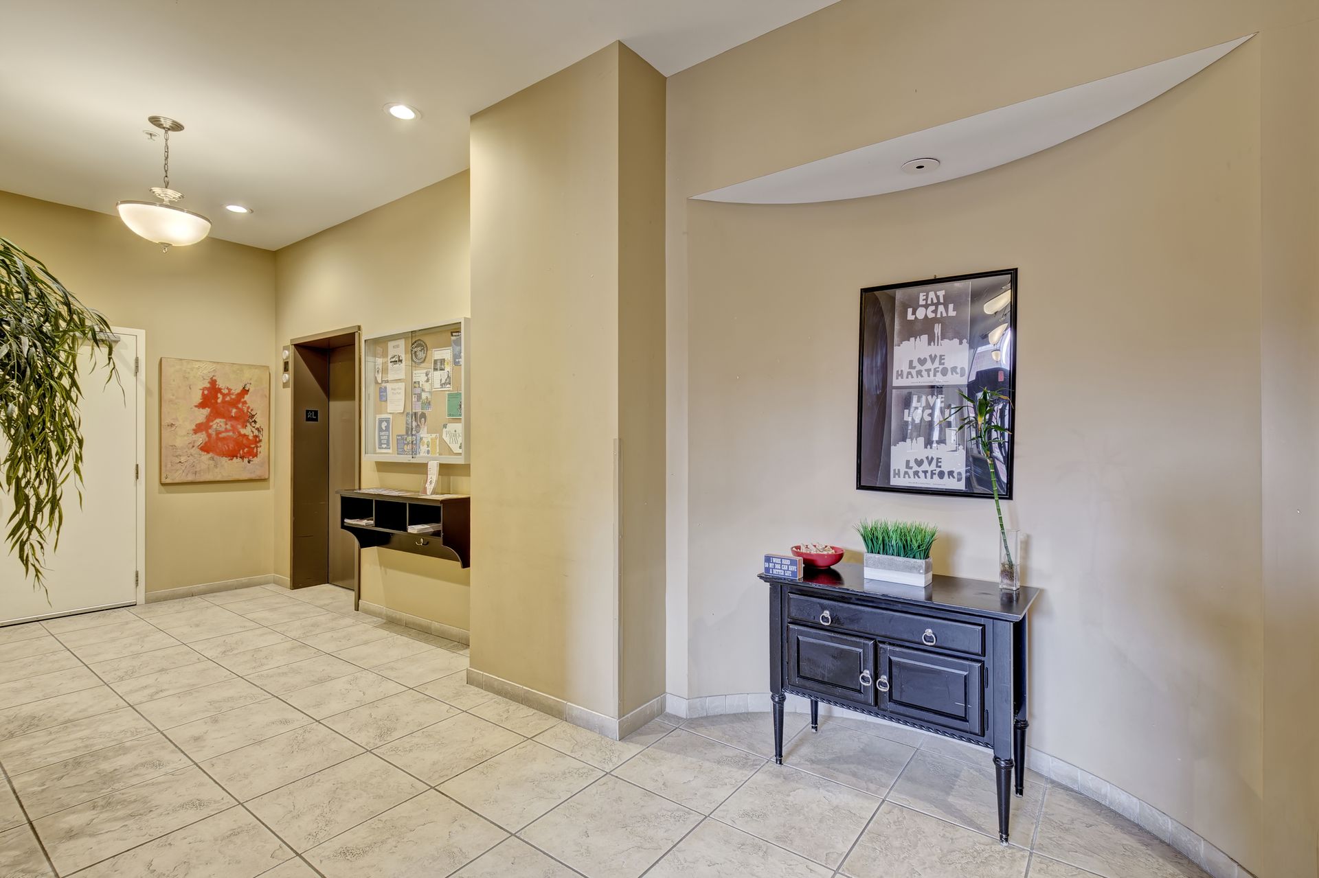 An entryway with beige walls, tiled floor, and a dark cabinet. Art and a plant decorate the space.