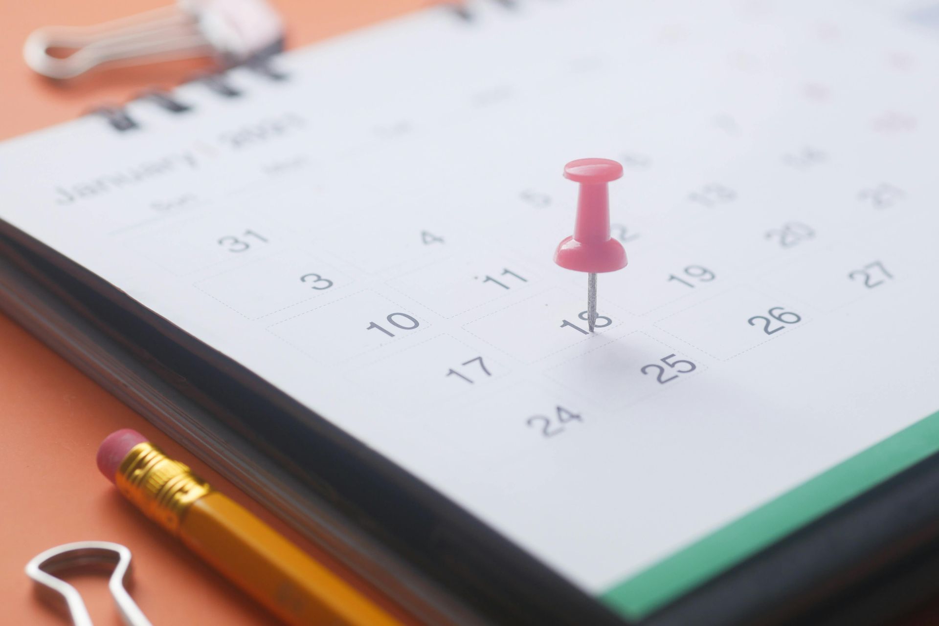 Close-up of a desk calendar, open to January, with a red push pin on the 16th.