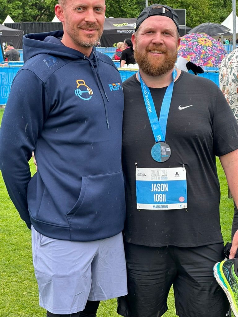 Ray and client Jason are posing for a picture in a field . one of the men has a medal around his neck.