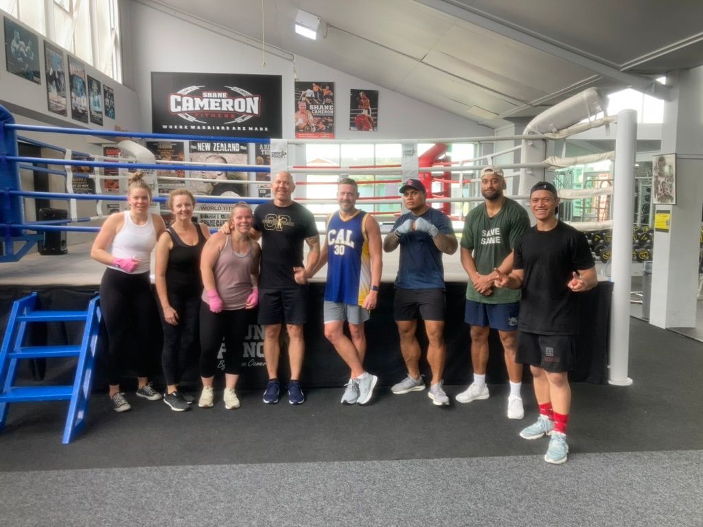 Ray and a group of people are posing for a picture in front of a boxing ring.