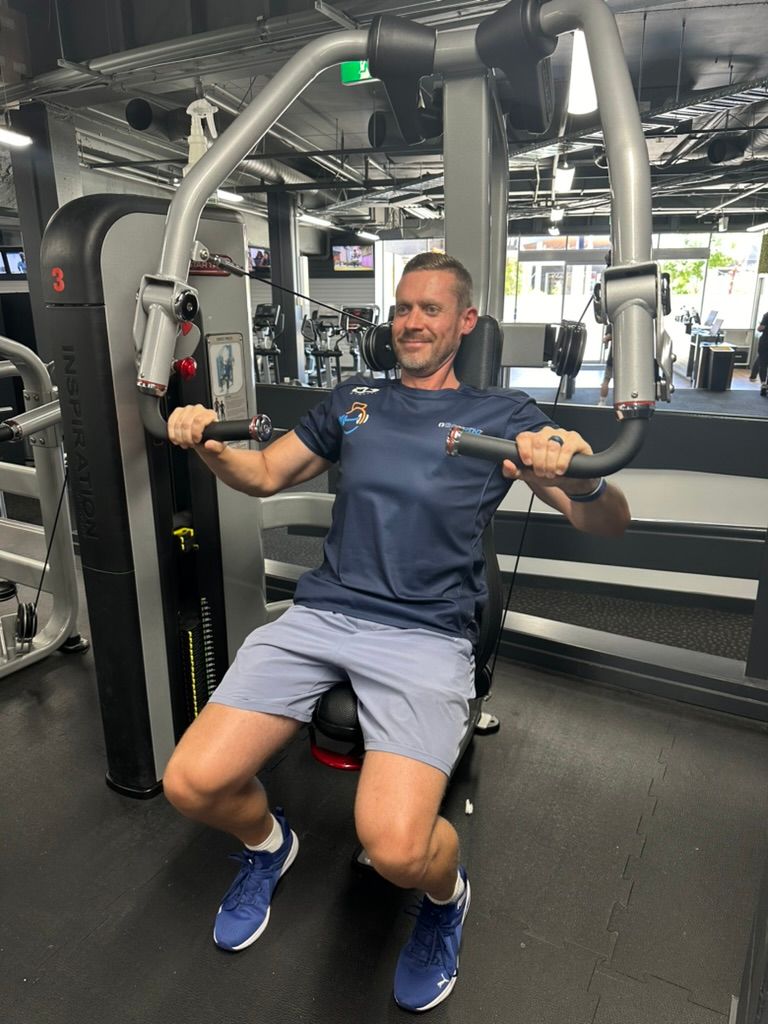 Ray is sitting on a machine in a gym.
