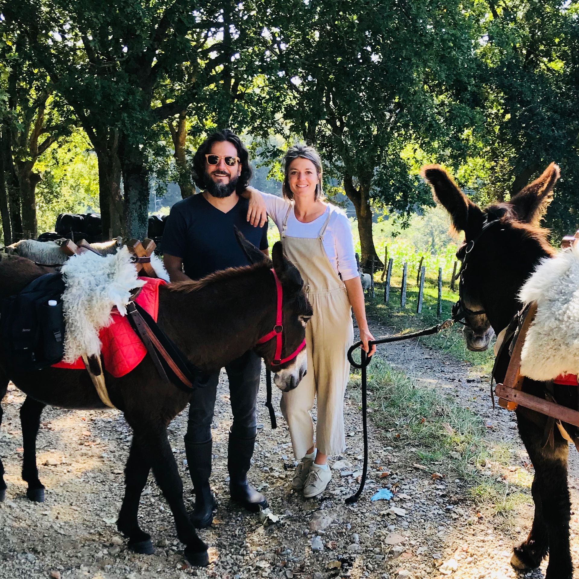 Man and woman standing with donkeys, trees in background.