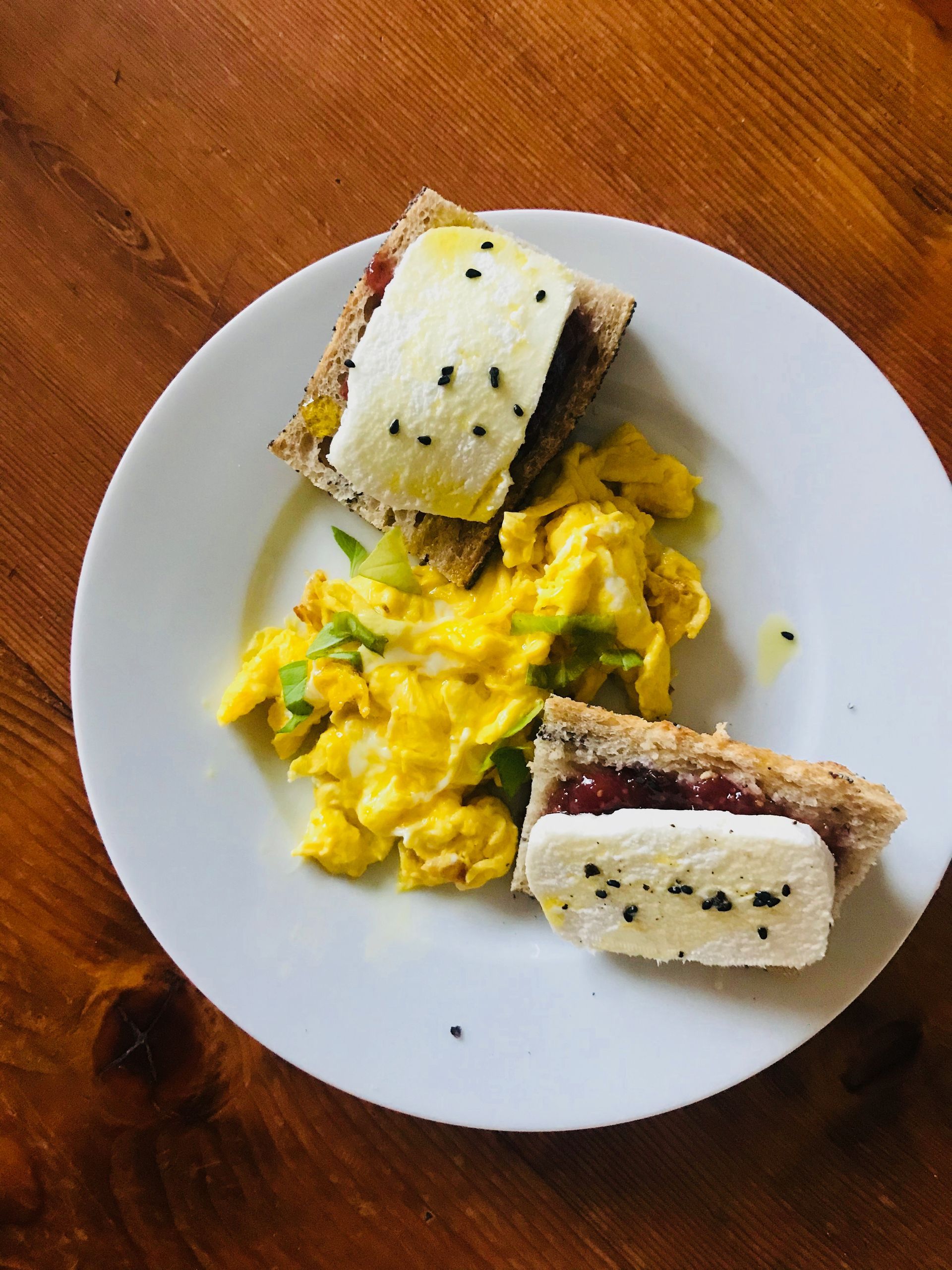 Breakfast plate: Scrambled eggs, two sandwiches with a white cheese and a jelly-like spread.