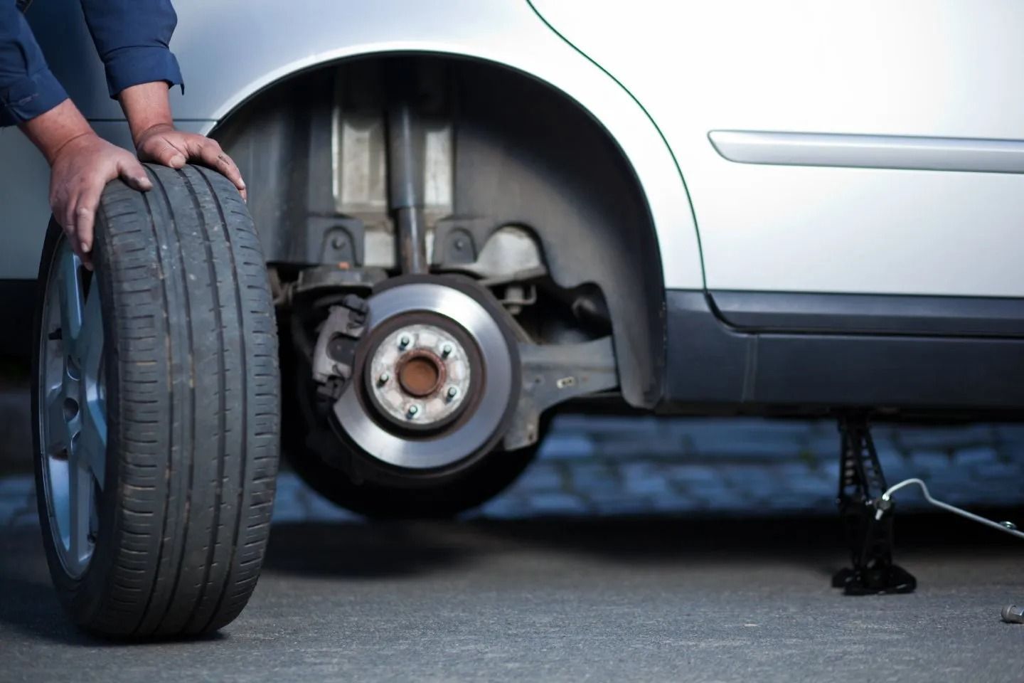 Persona che cambia la gomma di un'auto, tenendo la nuova gomma vicino al disco del freno esposto.