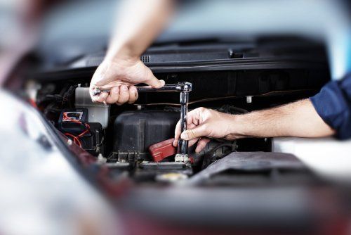 Mani che lavorano sul motore di un'auto con una chiave inglese.