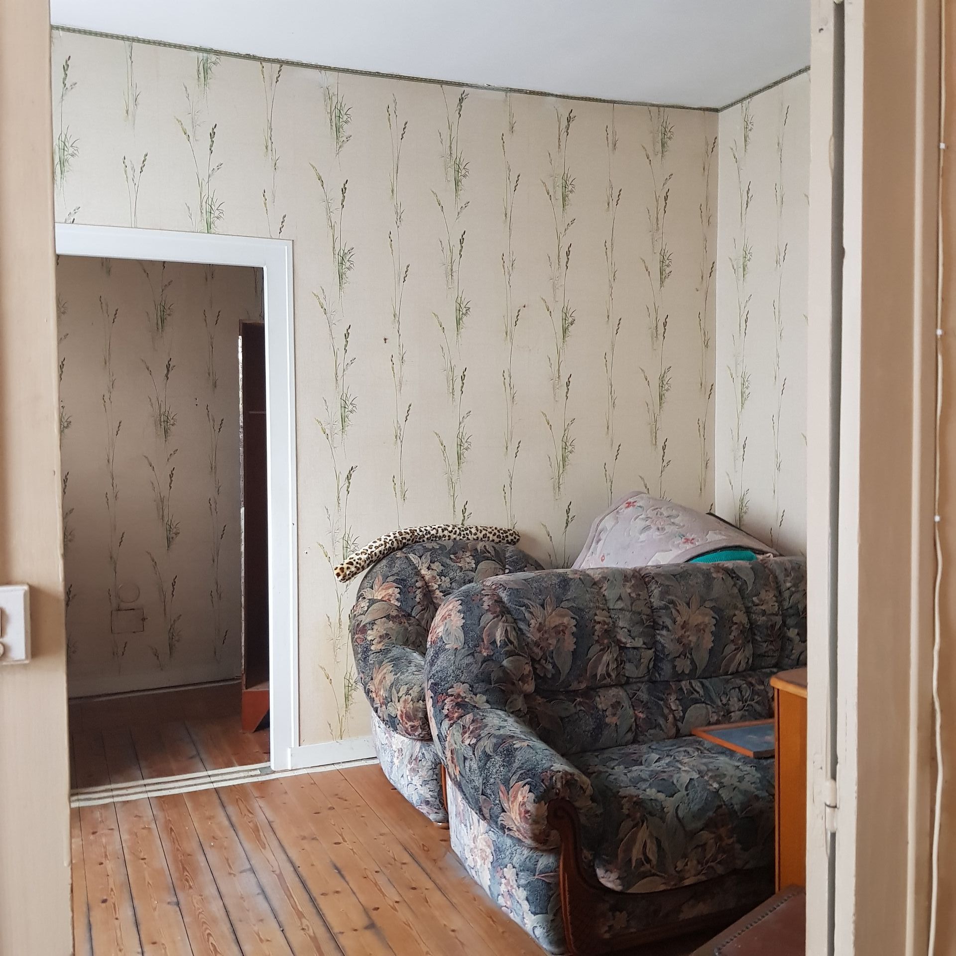 bedroom before renovation with yellowed wallpaper and an old sofa