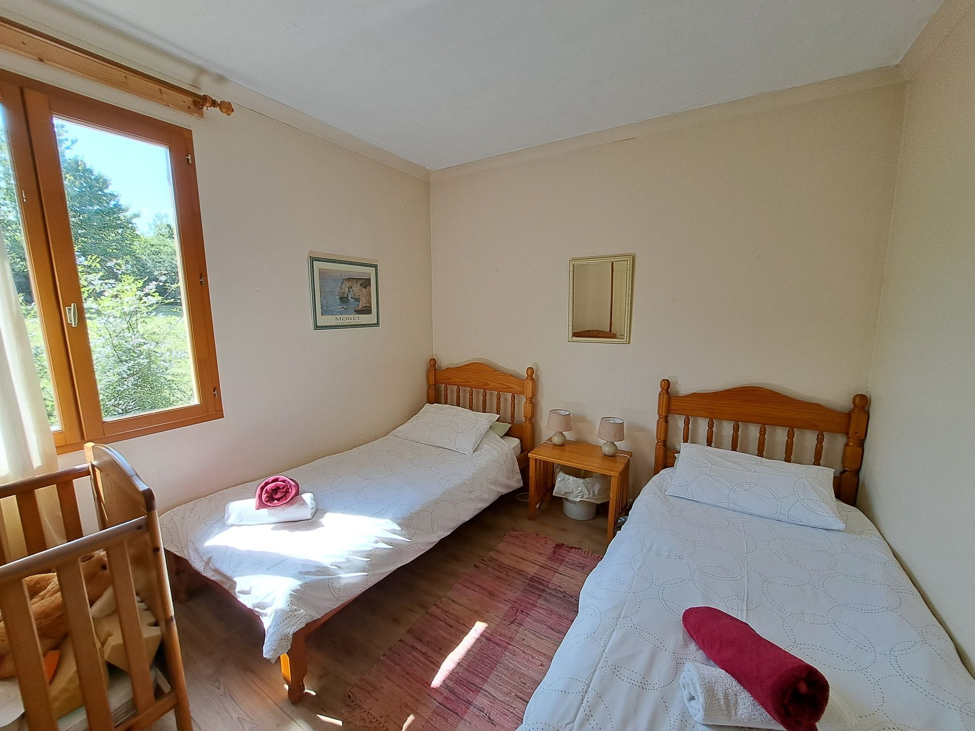 two pine single beds and a wooden pine cot in a room with cream walls and a window looking out over a garden