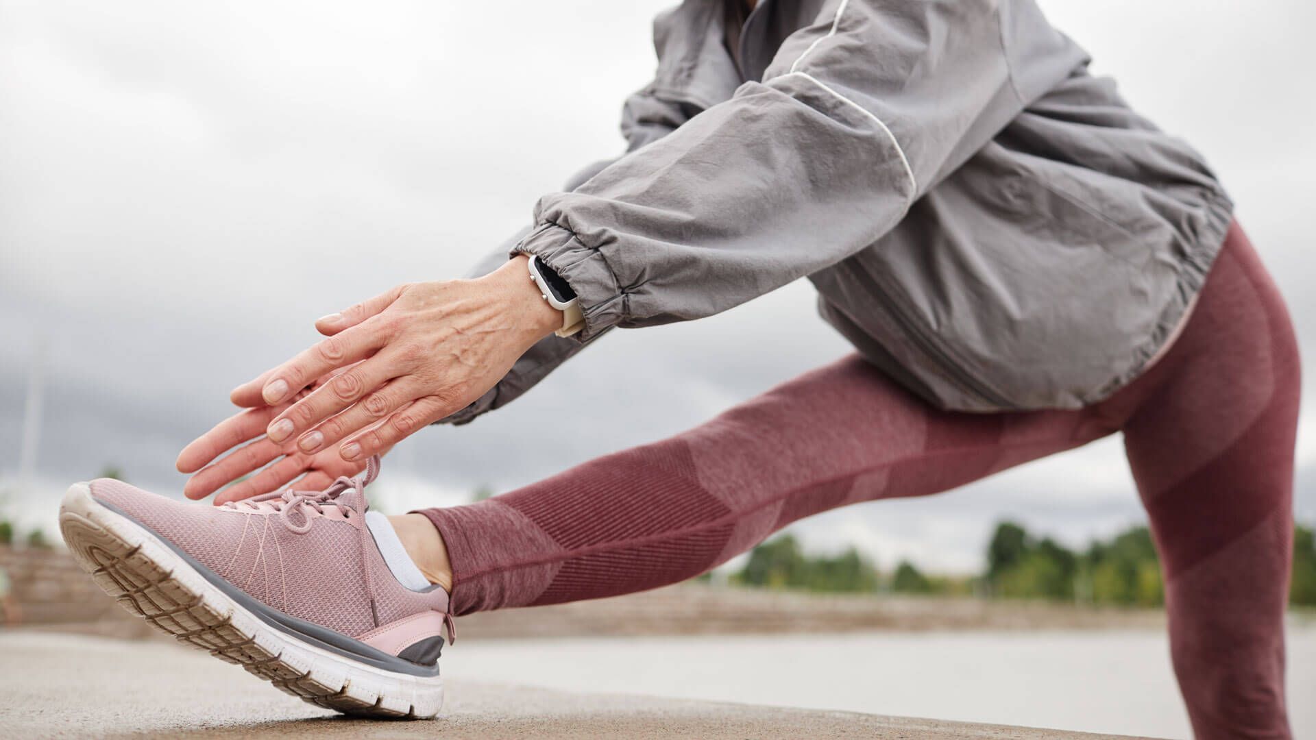 Person stretching outdoors in pink leggings and sneakers, reaching toward extended foot on a concrete surface