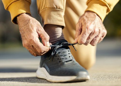 Hands tying the laces of a black running shoe on a pavement.