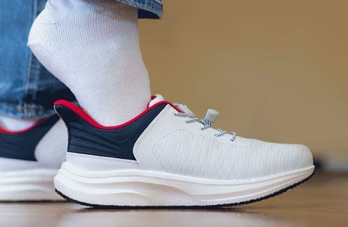 White sneaker with red and black accents on a foot wearing a white sock, close-up side view