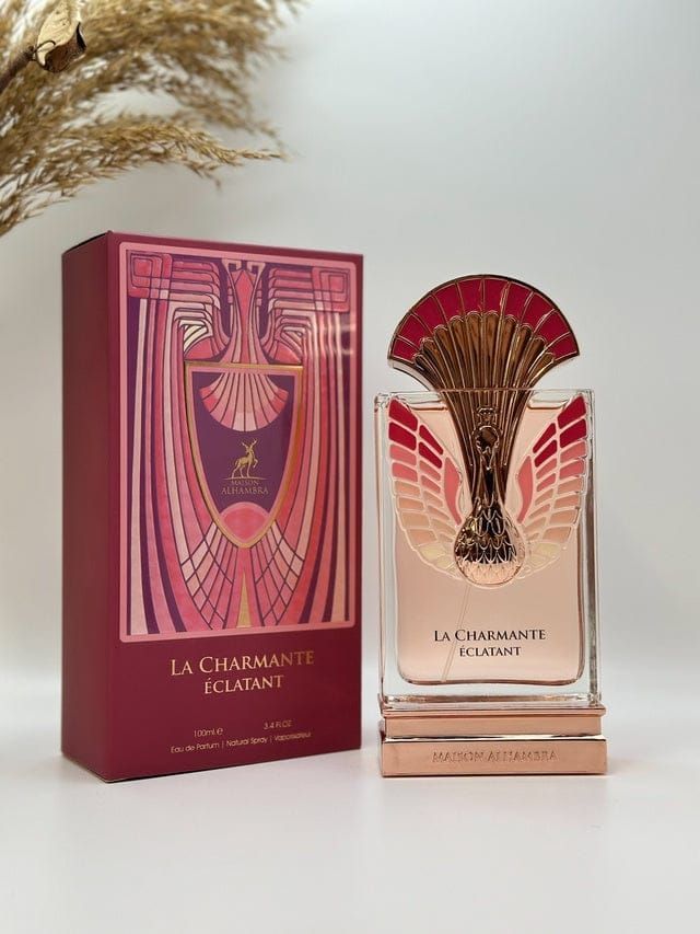 Frasco de perfume y caja roja a juego sobre fondo claro con diseño decorativo dorado y rosa.